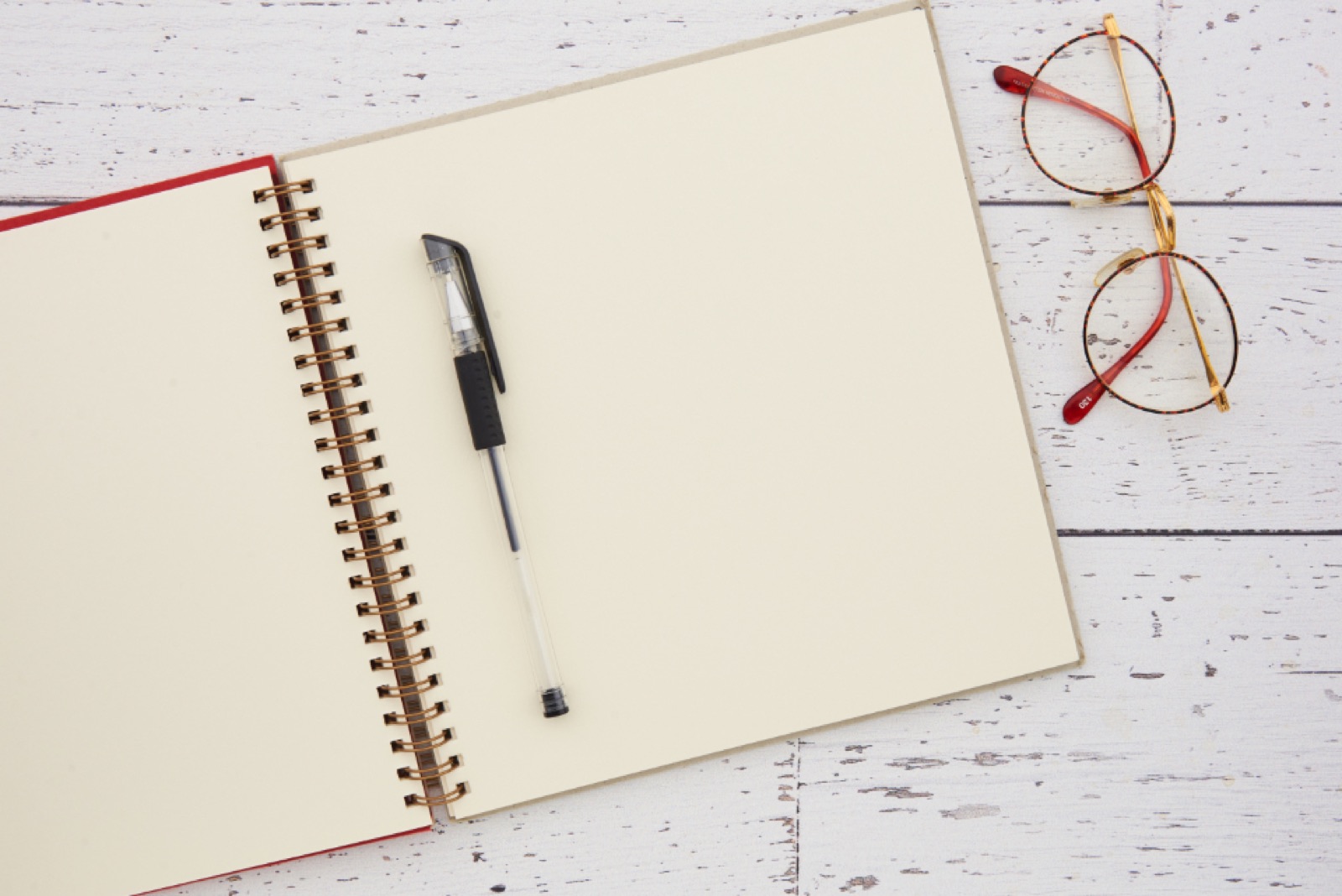 An open notebook, pen, and glasses on a desk